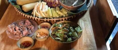 Una mesa de madera con diversos alimentos, entre ellos una cesta de maíz, un tazón de arroz y varios recipientes pequeños con salsas.