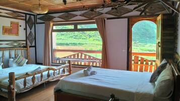 A room with two wooden beds, a wooden ceiling, and a view of a lush green landscape through large windows.