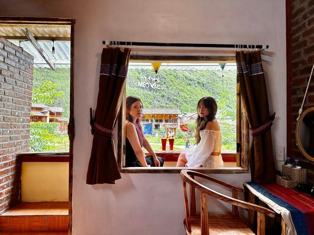Una habitación con ventana que da a un paisaje verde exuberante, un banco de madera y una pequeña mesa con un espejo y cestas.
