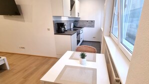 Una cucina compatta con mobili bianchi, una piccola zona pranzo con tavolo e sedie in vimini, e una finestra che offre vista all'esterno.