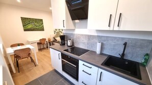 Una cucina compatta con mobili bianchi, un piano di lavoro nero e un forno integrato. C'è una zona pranzo con tavolo e sedie, e un quadro appeso al muro.