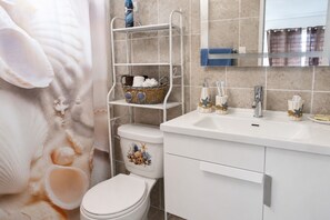 Un baño con inodoro, lavamanos y estante con artículos de tocador.