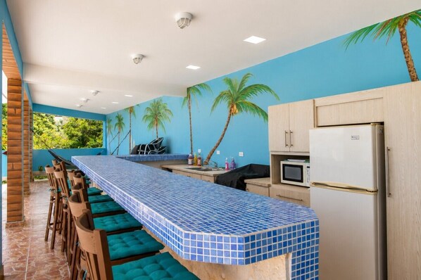 Una cocina con una encimera amplia, taburetes de bar, un refrigerador y un microondas.