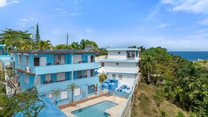 Un immeuble à plusieurs étages doté d’une piscine, entouré d’une végétation luxuriante et offrant une vue sur la mer.