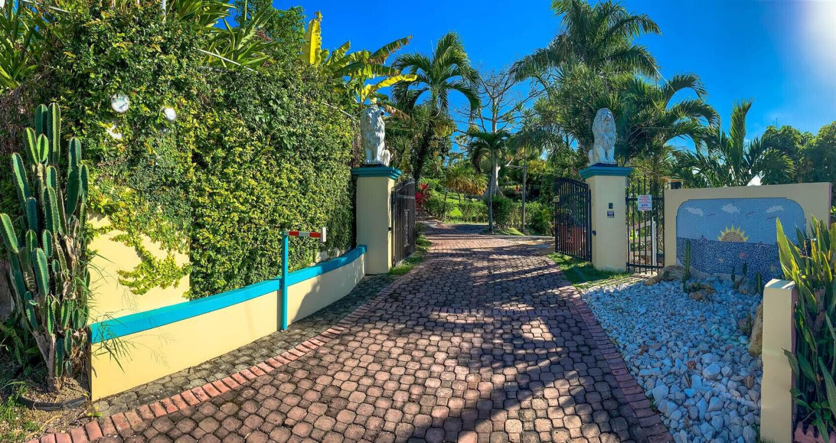 Un camino pavimentado que conduce a una entrada con puerta de reja, con una estatua a cada lado.