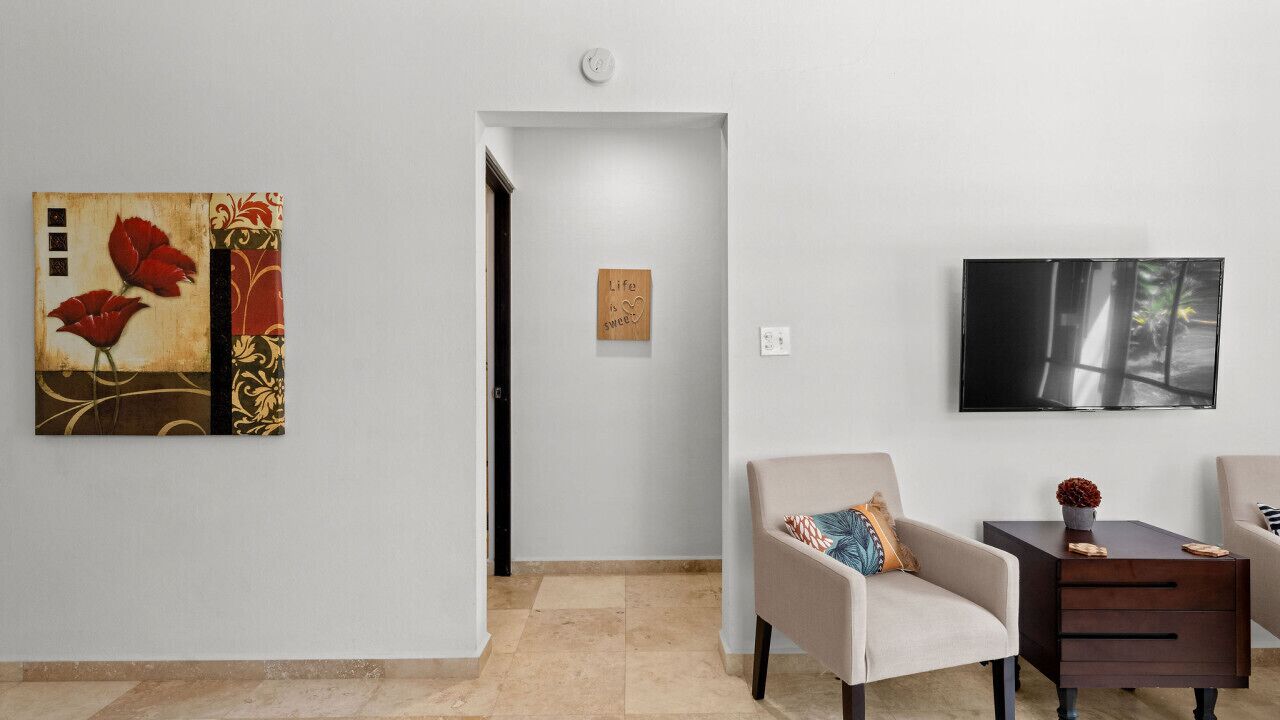 A modern living room with a beige armchair, a dark wooden side table, and a flat-screen TV mounted on the wall.