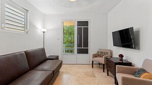 A modern living room with a brown leather sofa, a beige armchair, a small side table, and a flat-screen TV mounted on the wall. - Casita 4 at Ceiba Tree Inn (Rincón)