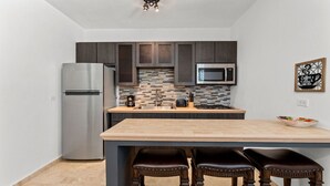 A modern kitchen with dark cabinets, a stainless steel refrigerator, a microwave, and a tiled backsplash. - Casita 4 at Ceiba Tree Inn (Rincón)