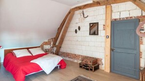 A bedroom with a sloped ceiling, a bed with red bedding, a wooden headboard, a blue door, and a small table with a lamp. - Cosy, country-style 3* gîte in the heart of Picardy's heritage, sleeps 5 (Mesbrecourt-Richecourt)