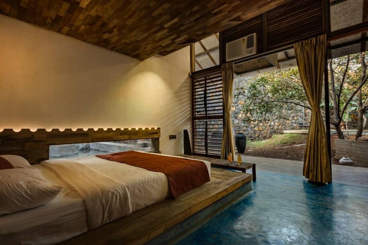 A bedroom with a bed, wooden headboard, and a view of a garden through a window.