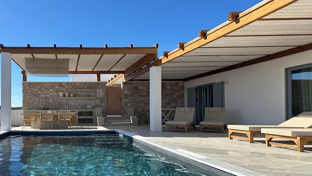 Un área de piscina con pared de piedra, mobiliario exterior y una pérgola.