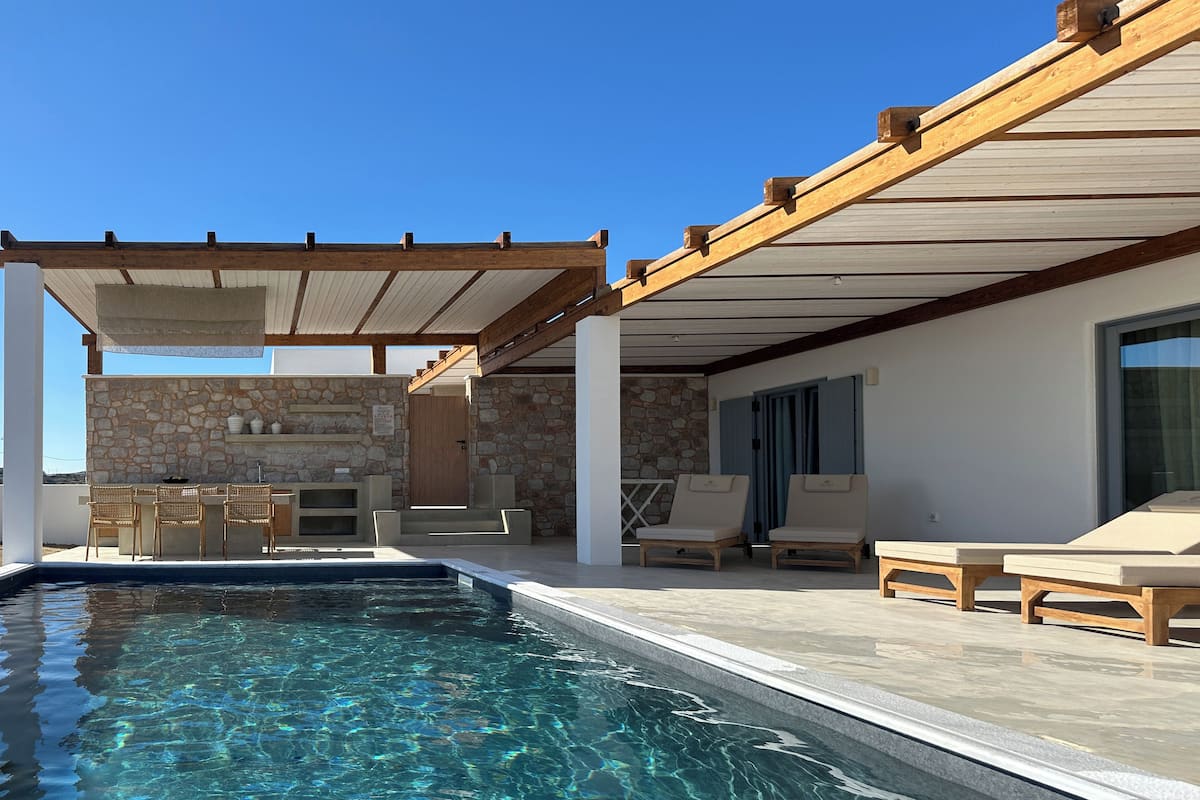 Un área de piscina con pared de piedra, mobiliario exterior y una pérgola.