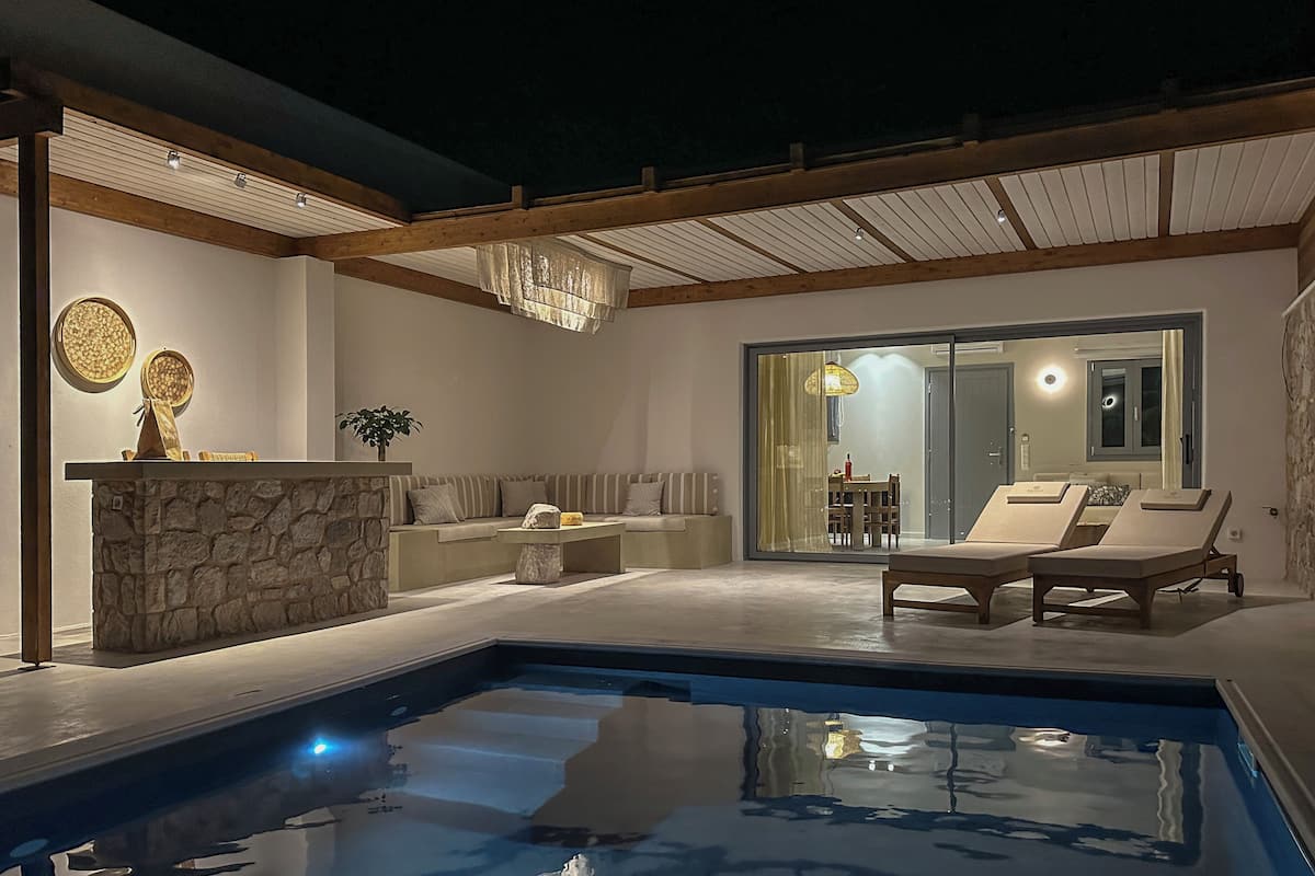 Un área de piscina moderna al aire libre con una chimenea de piedra, un sofá y sillones de descanso.