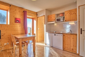 Ambiente interno in legno con tavolo da pranzo, sedie, microonde, lavastoviglie e finestra con tende.