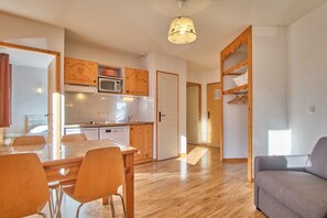 Eine moderne Küche mit Holzausbau, einem Esstisch mit Stühlen, einem grauen Sofa und einer Pendelleuchte.