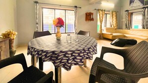 A dining area with a round table, chairs, a vase with flowers, and a sofa in the background.
