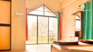 A hotel room with a large sliding glass door leading to an outdoor area, a bed, a small table, and a bench.