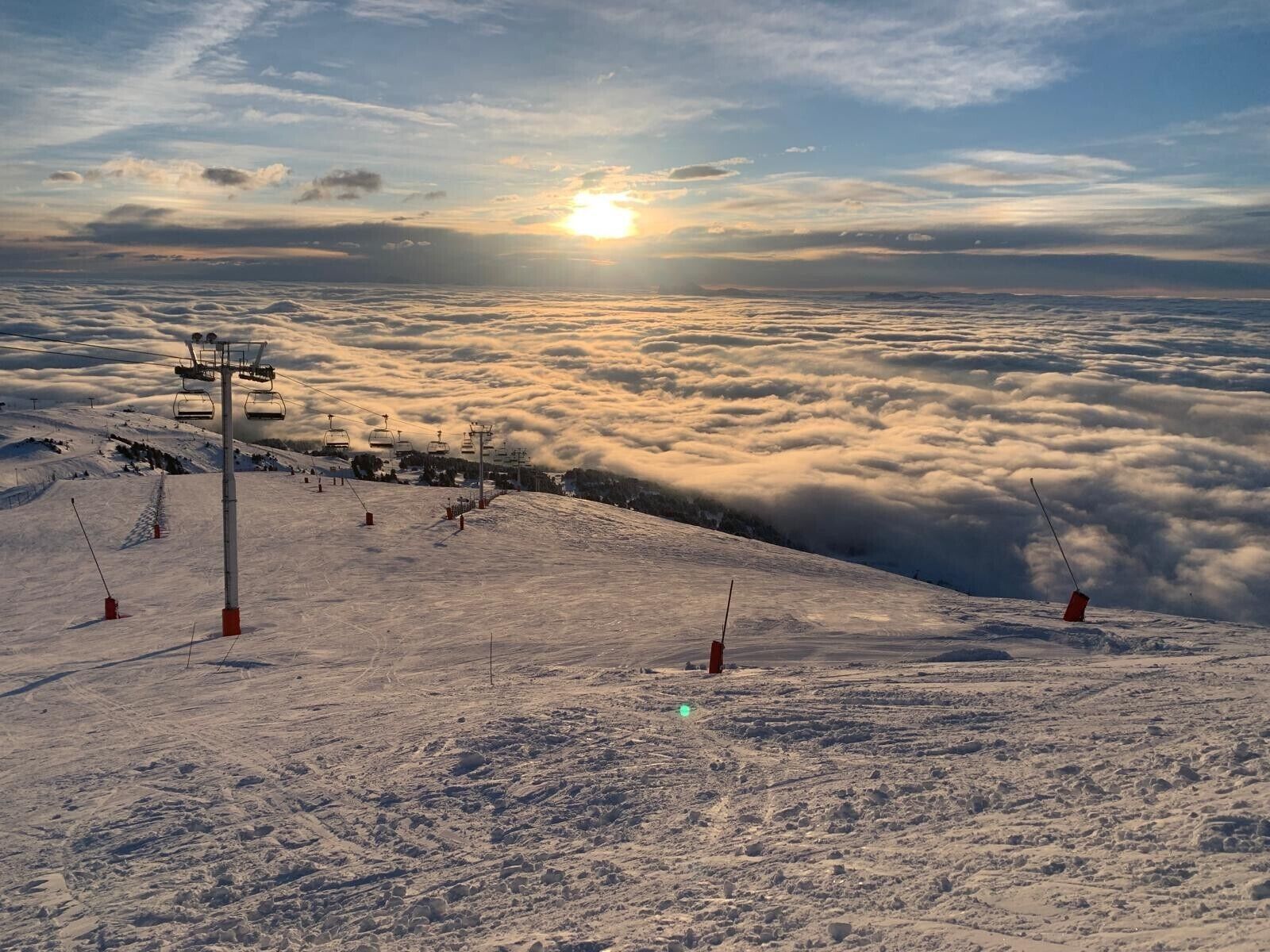 Eine verschneite Berglandschaft mit einer Seilbahn, blauem Himmel und untergehendem oder aufsteigendem Sonnenlicht.