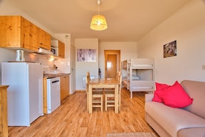 Un espacio habitable compacto con suelo de madera, kitchenette, zona de comedor y un sofá con un cojín rojo.