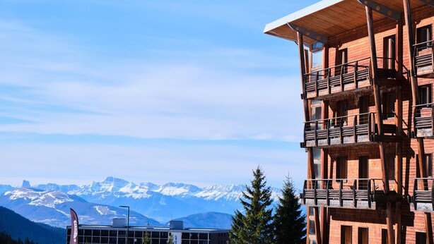 Ein mehrstöckiges Gebäude mit Balkonen, im Hintergrund Berge und ein klarer Himmel.