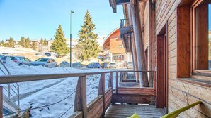 Un bâtiment en bois doté d’une terrasse en bois, d’une chaise jaune et offrant une vue sur les voitures garées et les arbres.