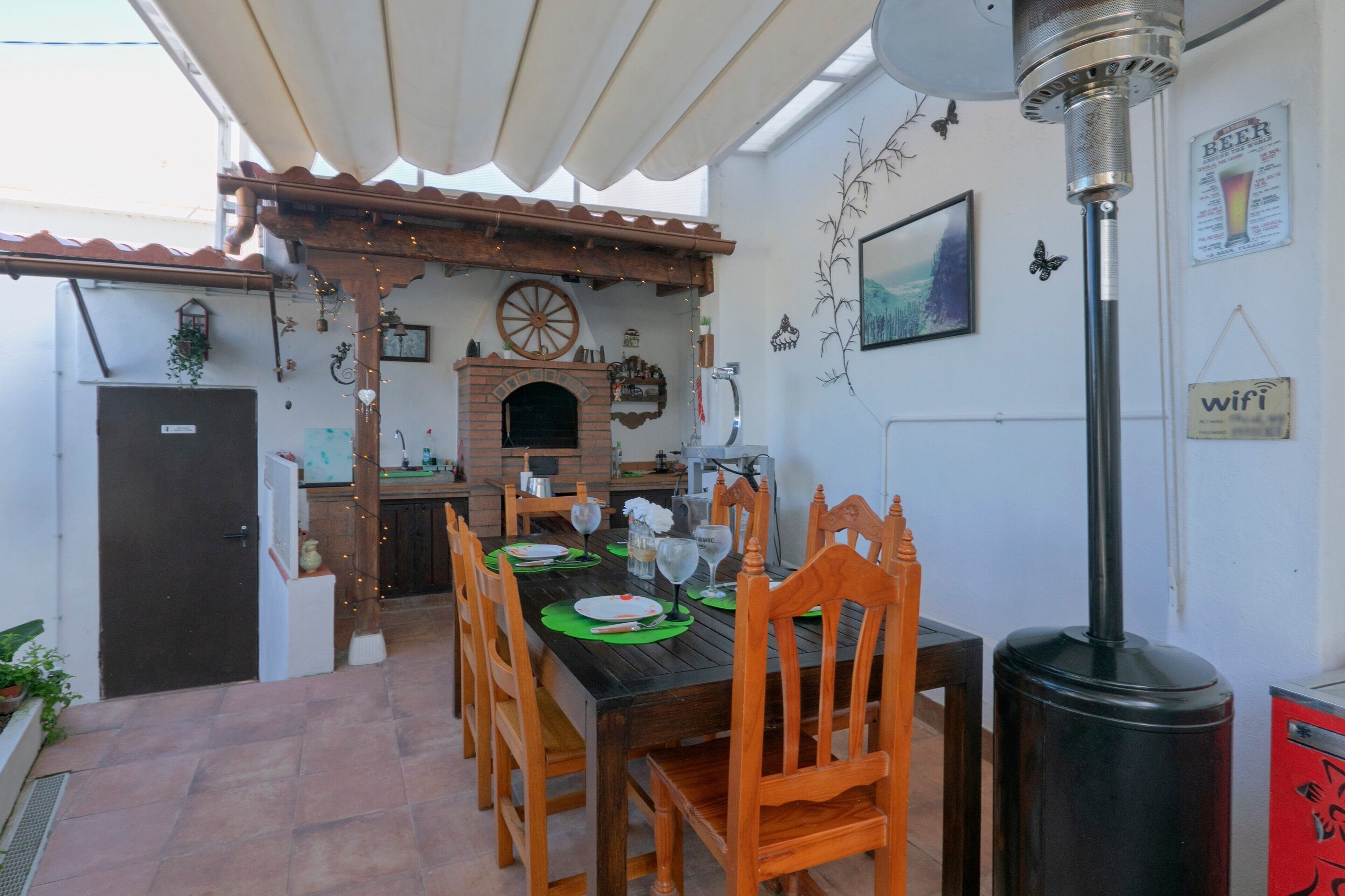 Un comedor con una mesa dispuesta para seis personas, rodeada de sillas de madera, una chimenea de ladrillo y un ventilador de techo.