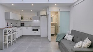 Une cuisine moderne avec des meubles blancs, un coin repas avec des chaises blanches et un canapé gris agrémenté de coussins à motifs.