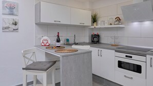 Une cuisine moderne avec des armoires blanches, un four encastré et un coin repas comprenant une chaise et une table blanches.