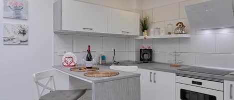 A modern kitchen with white cabinets, a built-in oven, and a dining area with a white chair and table.