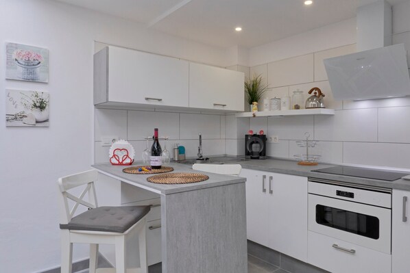 Una cocina moderna con armarios blancos, horno empotrado y zona de comedor con una silla y mesa blancos.
