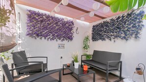 Un espace patio aménagé avec un canapé noir, deux chaises noires, une table en verre et une plante en pot.