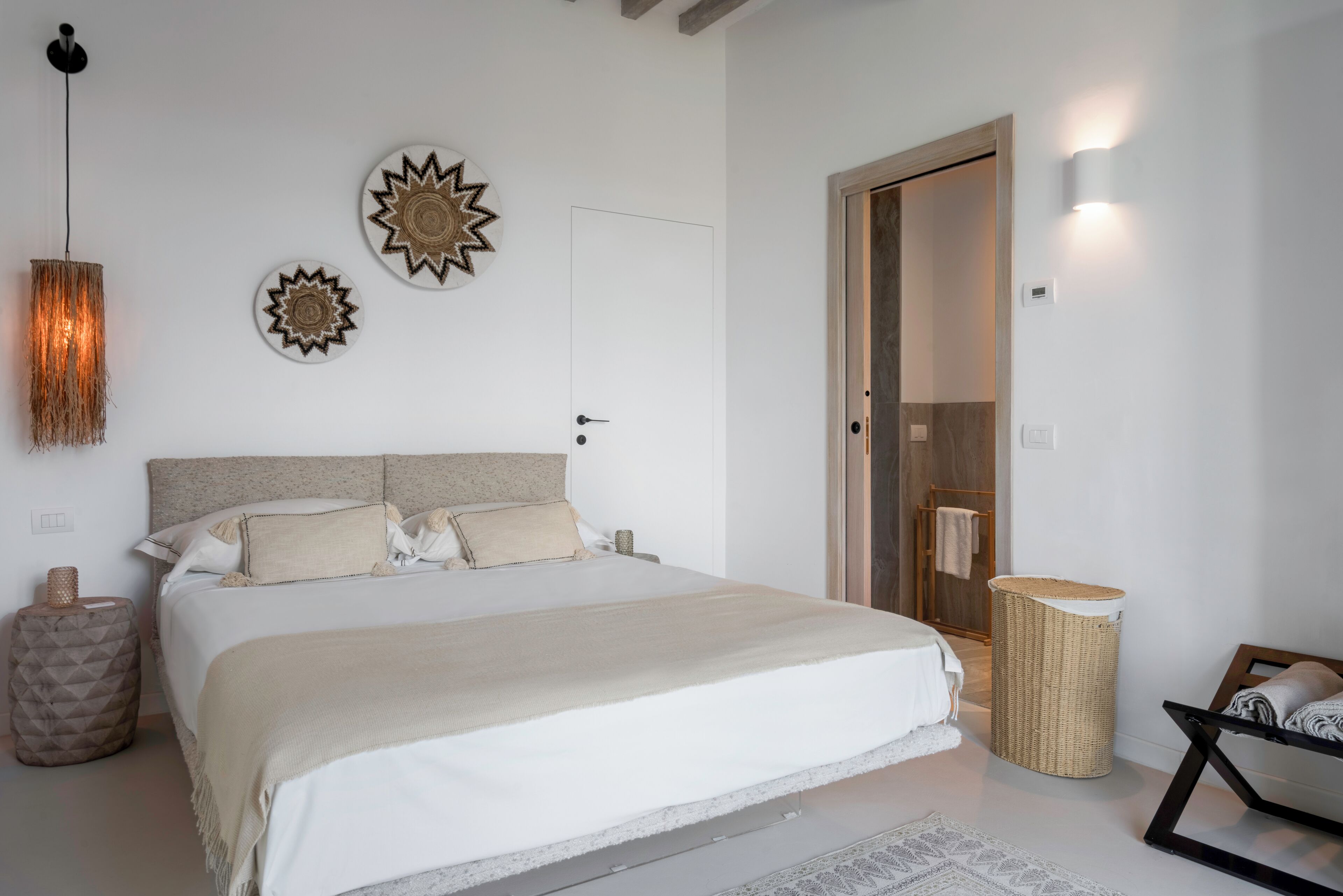 A bedroom with a large bed, a hanging light fixture, and decorative wall art.