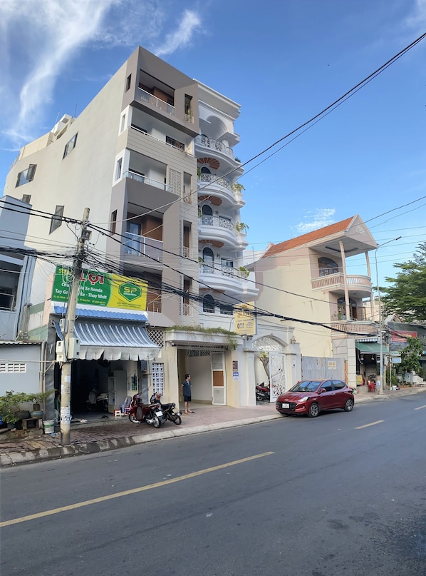 A multi-story building with a commercial ground floor, featuring a shop with a green sign and a red car parked outside. - Jolilian Hotel & Apartment (Ho Chi Minh City)