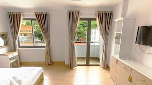 A bedroom with a bed, a desk, a TV, and a balcony with curtains. - Jolilian Hotel & Apartment (Ho Chi Minh City)