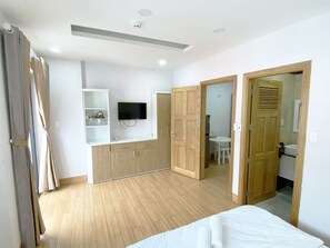 A bedroom with a bed, wooden wardrobe, a TV mounted on the wall, and a bathroom visible through an open door. - Jolilian Hotel & Apartment (Ho Chi Minh City)