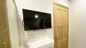 A room with a flat-screen TV mounted on the wall, a white counter with a telephone and bottled water, and a wooden door. - Jolilian Hotel & Apartment (Ho Chi Minh City)