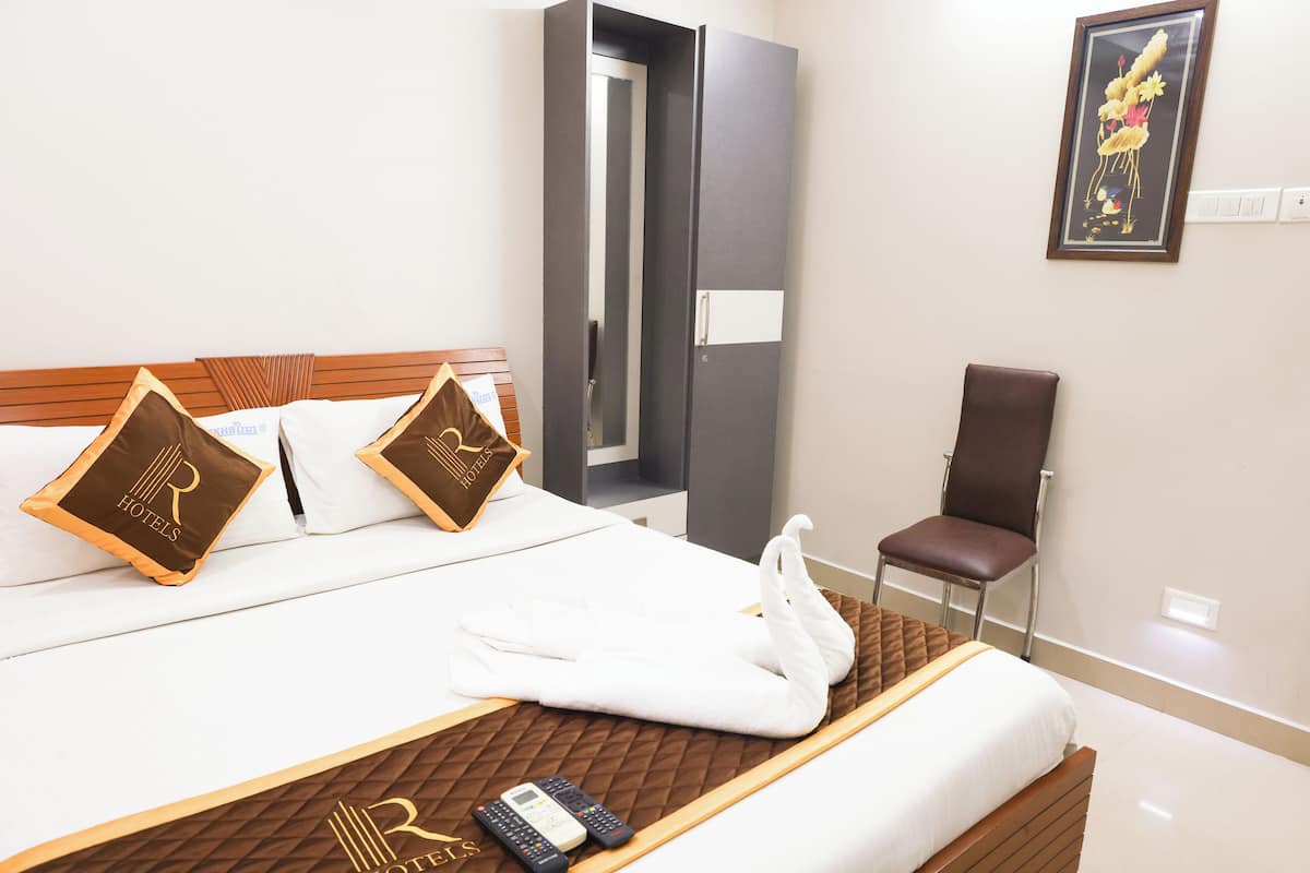 A hotel room with a bed, a chair, a robe, and a remote control.