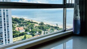A room with a large window offering a view of a beach and ocean, a tiled floor, and a curtain with a tree pattern. - Oasky Apartment Vung Tau (Ho Chi Minh City)