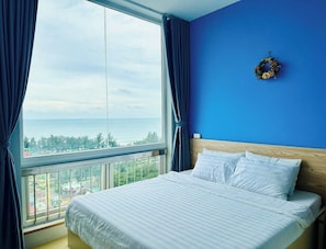 A hotel room with a large bed, a view of the sea, and a blue wall.
