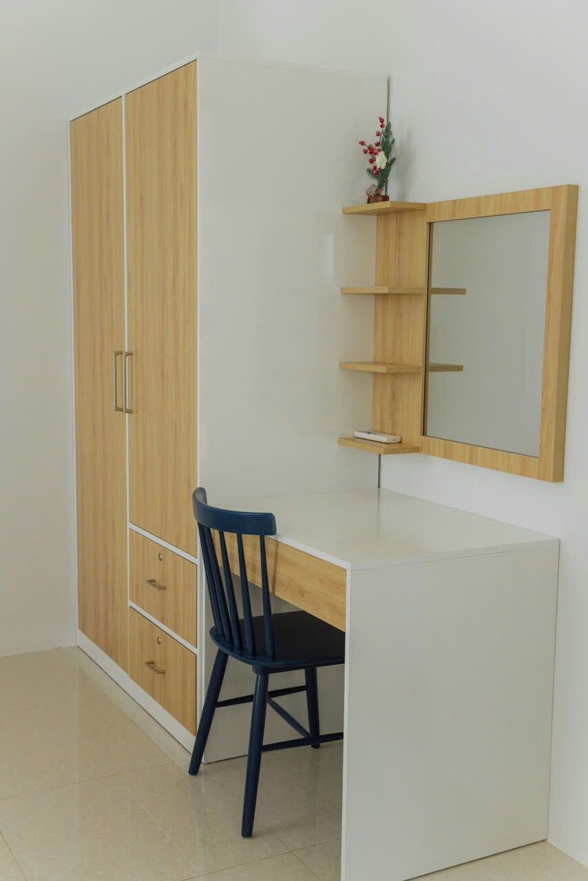 A room with a wooden wardrobe, a desk with a chair, and a wall-mounted shelf with a mirror.
