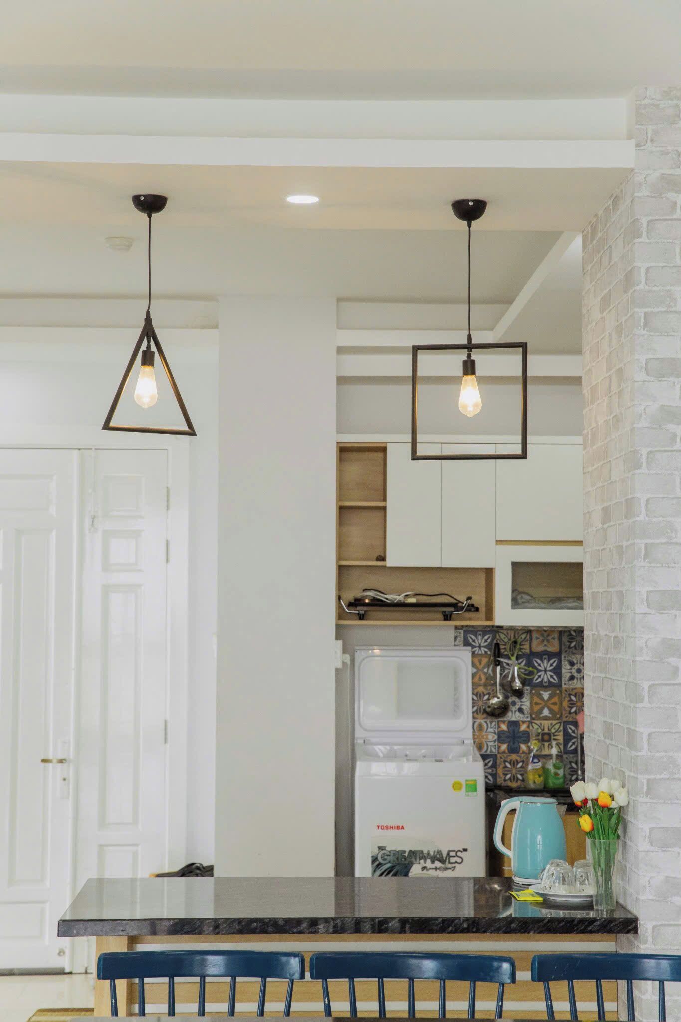 A modern kitchen with a black countertop, white cabinets, and a white refrigerator. There are two hanging pendant lights and a vase with flowers on the counter.