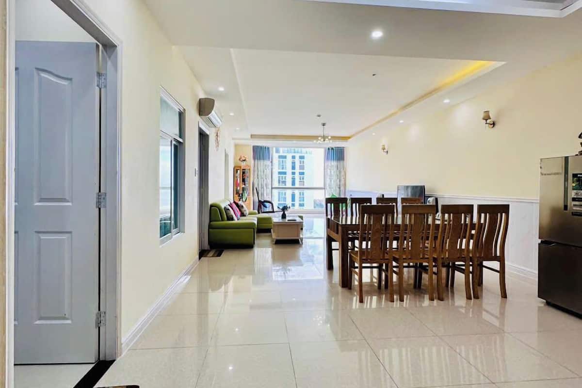 A spacious living area with a dining table and chairs, a sofa, and a kitchen area with a refrigerator.