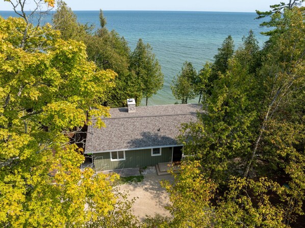 A house with a chimney, surrounded by trees and overlooking a body of water.