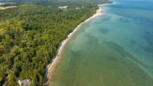 Vista aérea de una zona costera con un bosque denso, una playa arenosa y aguas azules cristalinas.