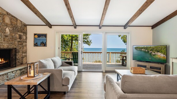 Un salón acogedor con chimenea de piedra, un sofá cómodo, un televisor y un balcón con vistas al mar.
