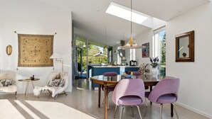 Ein moderner Essbereich mit hoher Decke, einem zentralen Tisch und violetten Stühlen.