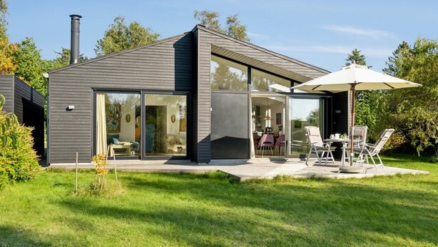 Ein modernes Haus mit Terrasse, komplett mit Tisch, Stühlen, einem großen Sonnenschirm und einem Schornstein.