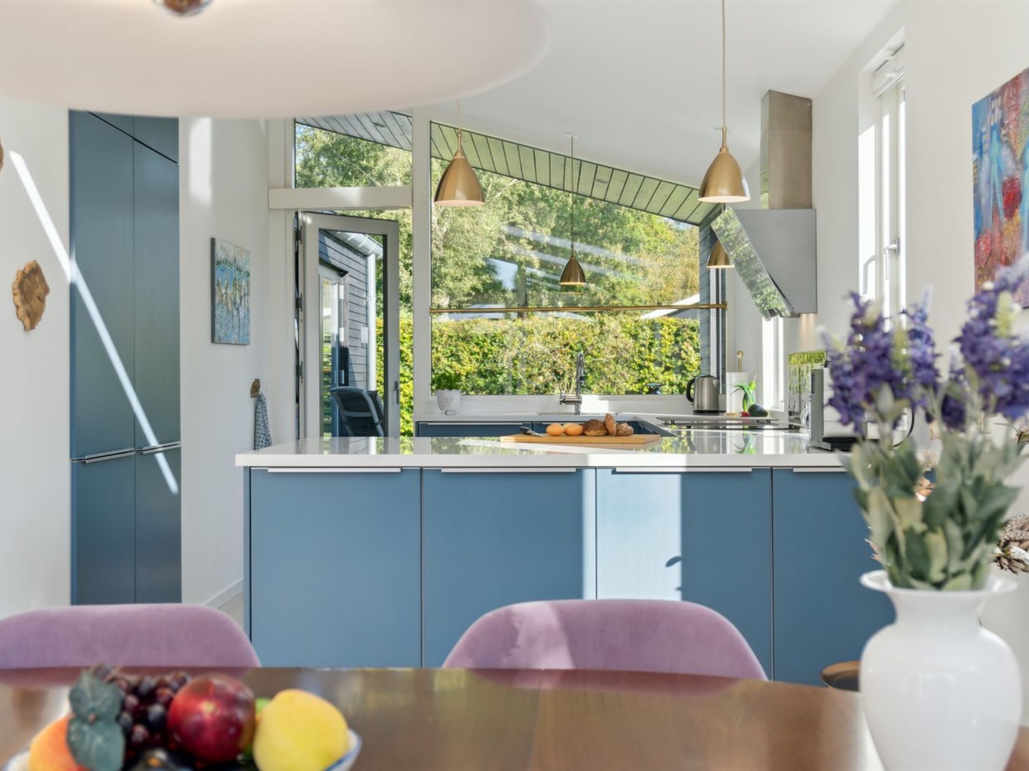 Een moderne keuken met blauwe kastjes, een groot raam en hanglampen.