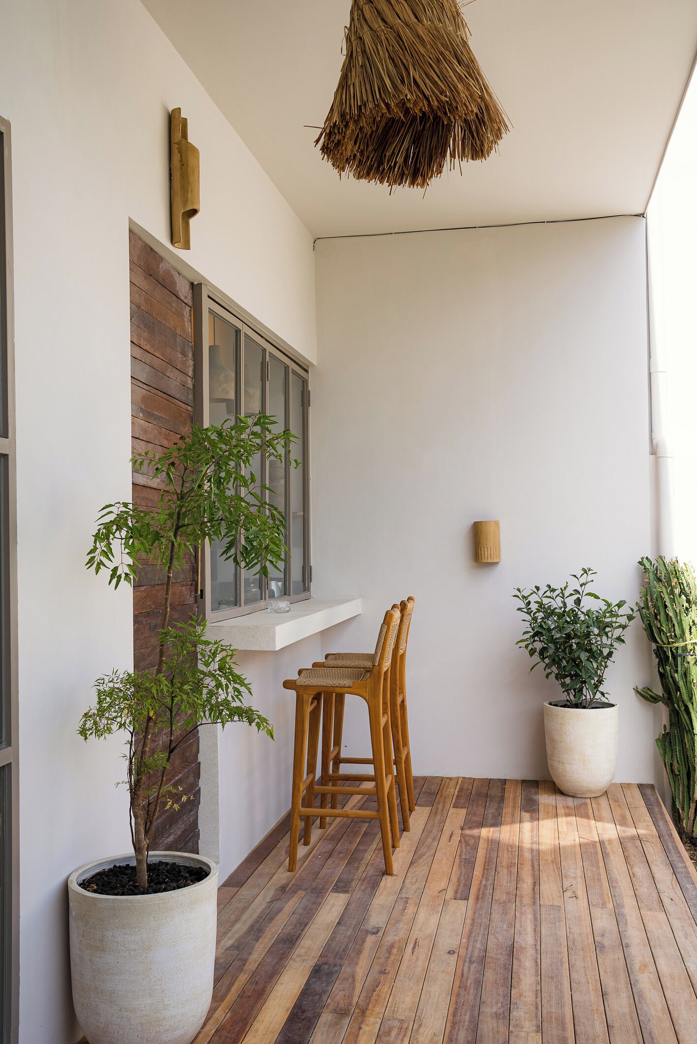 A small, cozy balcony with a wooden floor, a potted plant, a wooden chair, and a hanging light fixture.