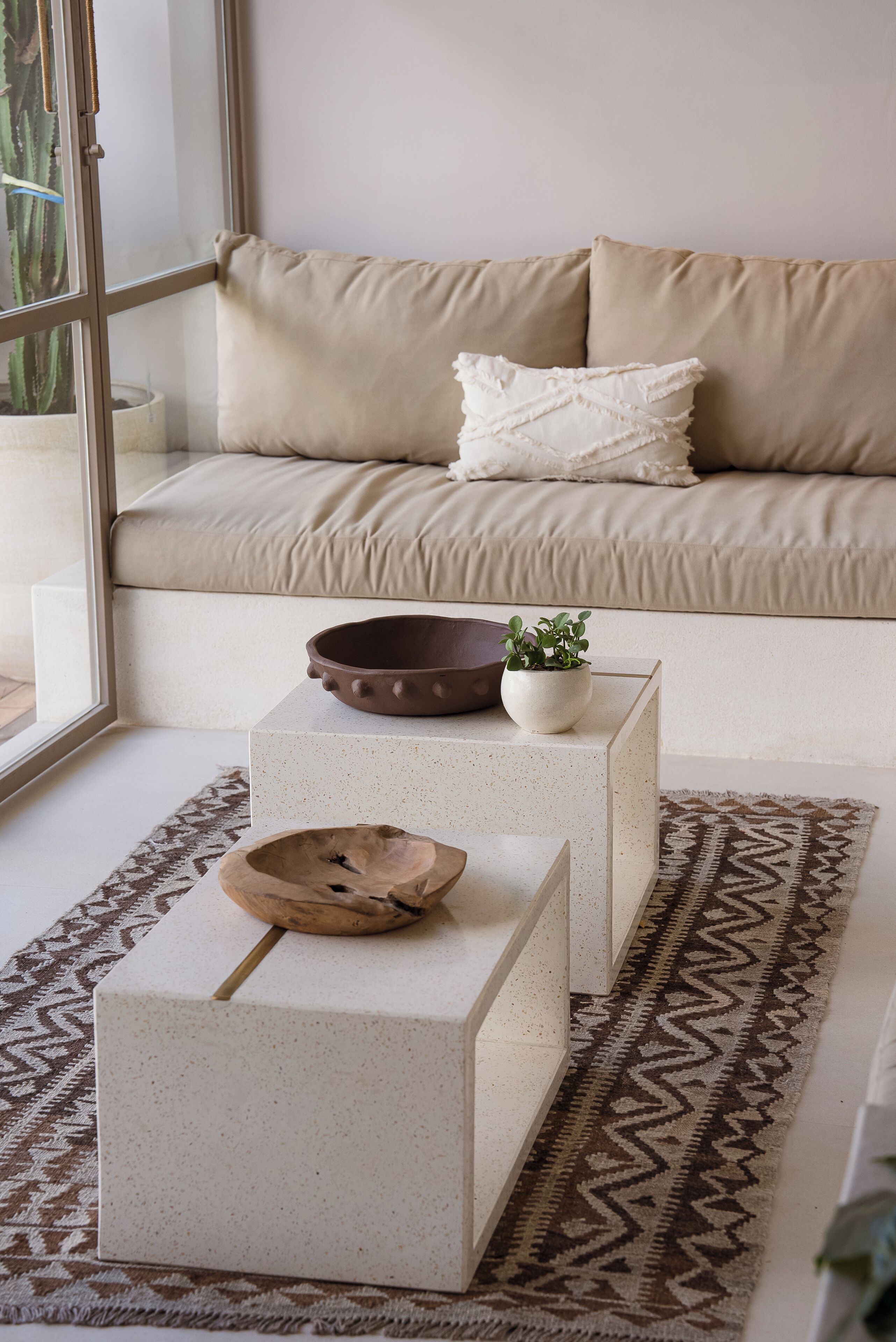 Ein modernes Wohnzimmer mit einem beigefarbenen Sofa, zwei weißen Beistelltischen und einem gemusterten Teppich.